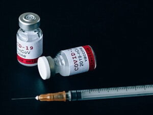 Two bottles of vaccine and a syringe over a black background