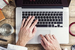 hands-of-person-typing on a-computer-on a wooden-desk-background