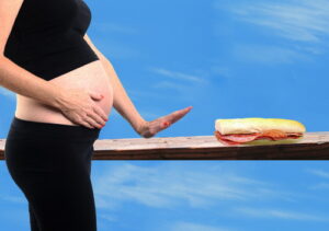 Pregnant woman putting up hand against eating deli meat sandwici